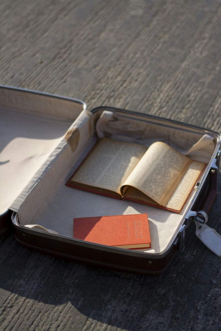 An open suitcase on a textured surface containing books, evoking travel and exploration themes.